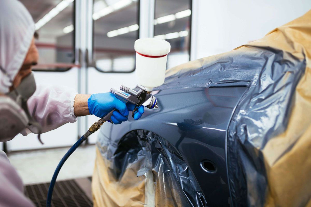 Peinture d'une voiture au pistolet par un homme en tenue